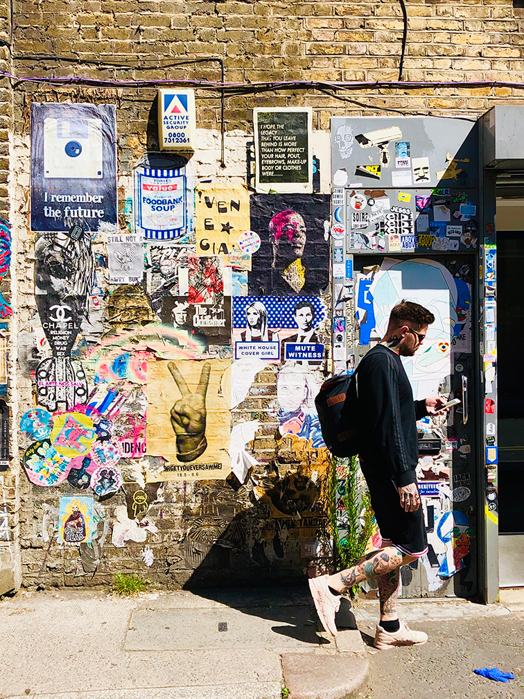 Person walking by a stone wall covered in posters and art in London, England